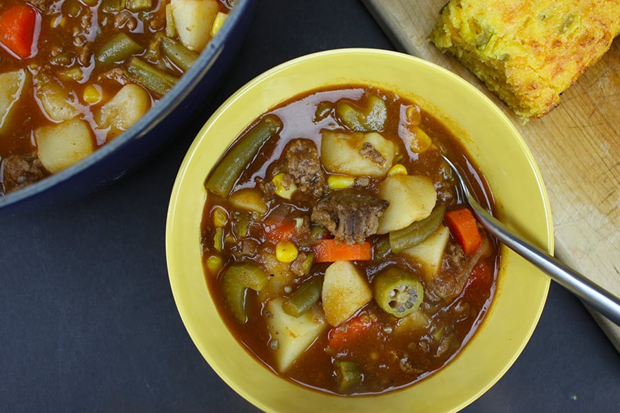 Vegetable beef soup with cornbread served in a yellow bowl.