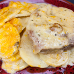 Smothered pork chops with potatoes on a red plate.