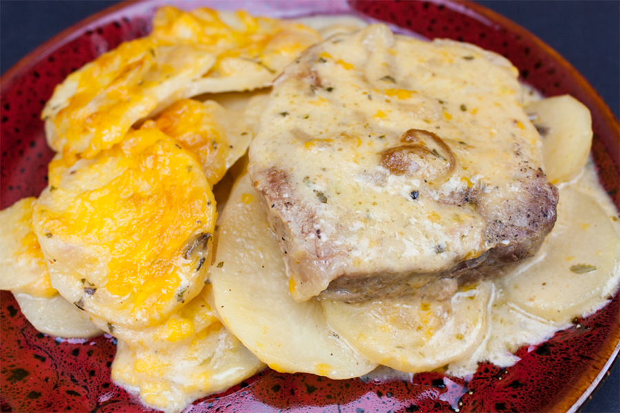 Smothered pork chops with potatoes on a red plate.