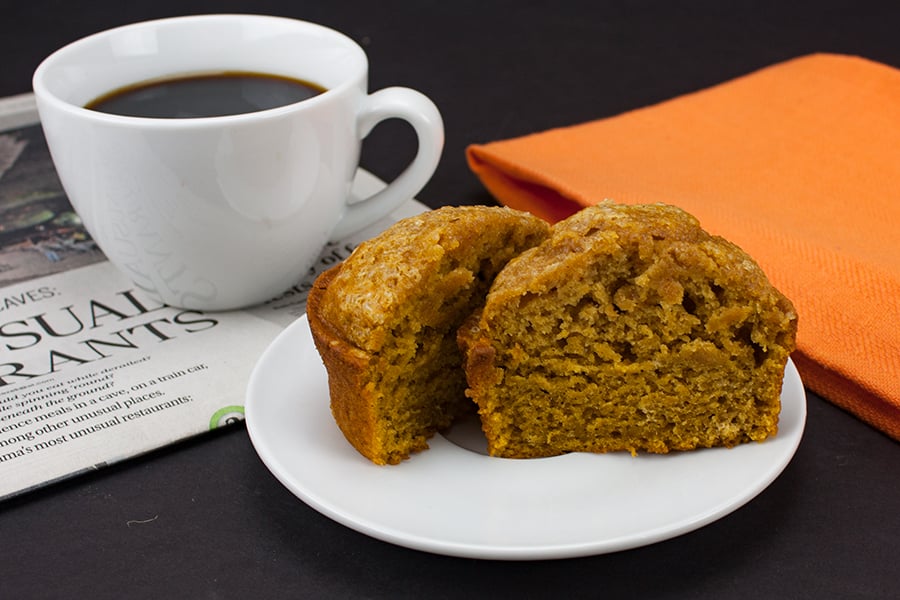 Bakery Style Pumpkin Muffin sliced in half on a white plate next to a white coffee mug