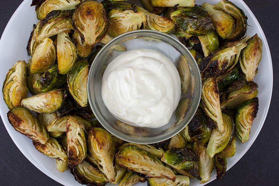 Roasted brussels sprouts with aioli in a glass ramekin.