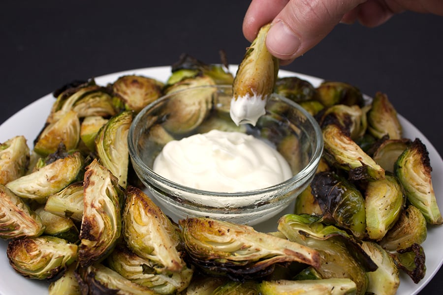 Roasted Brussel sprouts on a white plate with a glass ramekin of aioli.