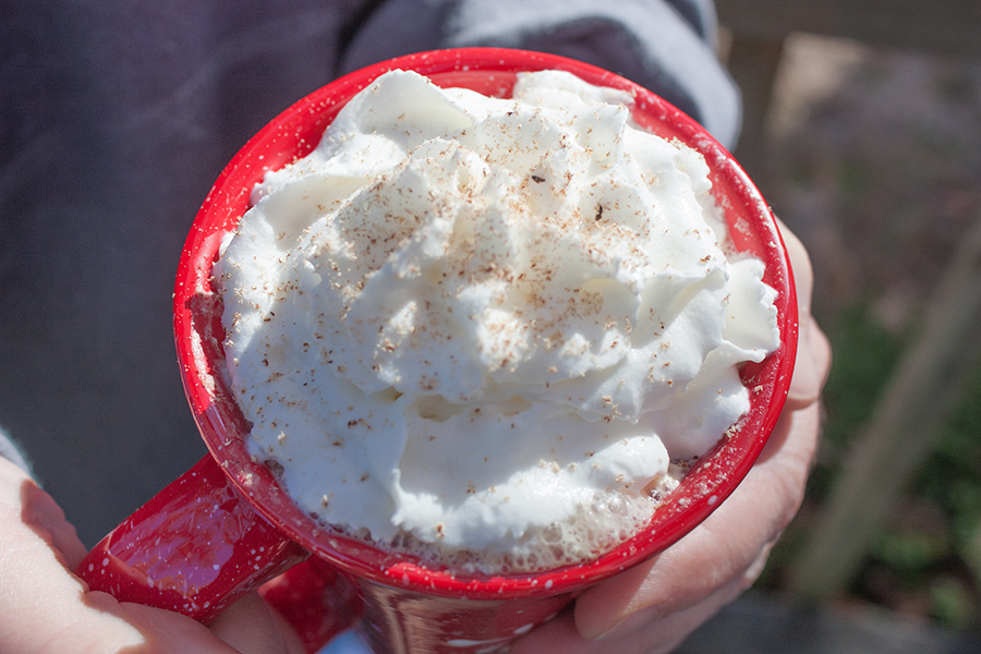 Eggnog latte being held in hands in a red mug with snowflake design.