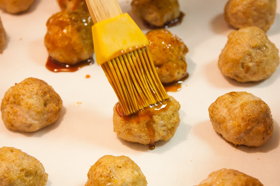 Baked firecracker chicken meatballs being brushed with sauce