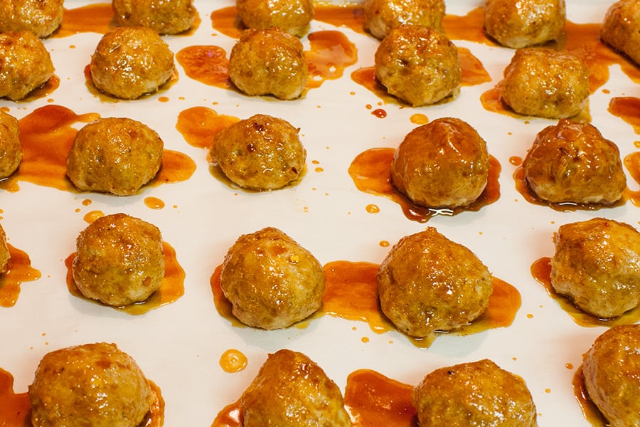 Firecracker chicken meatballs brushed with sauce on a parchment lined baking sheet.