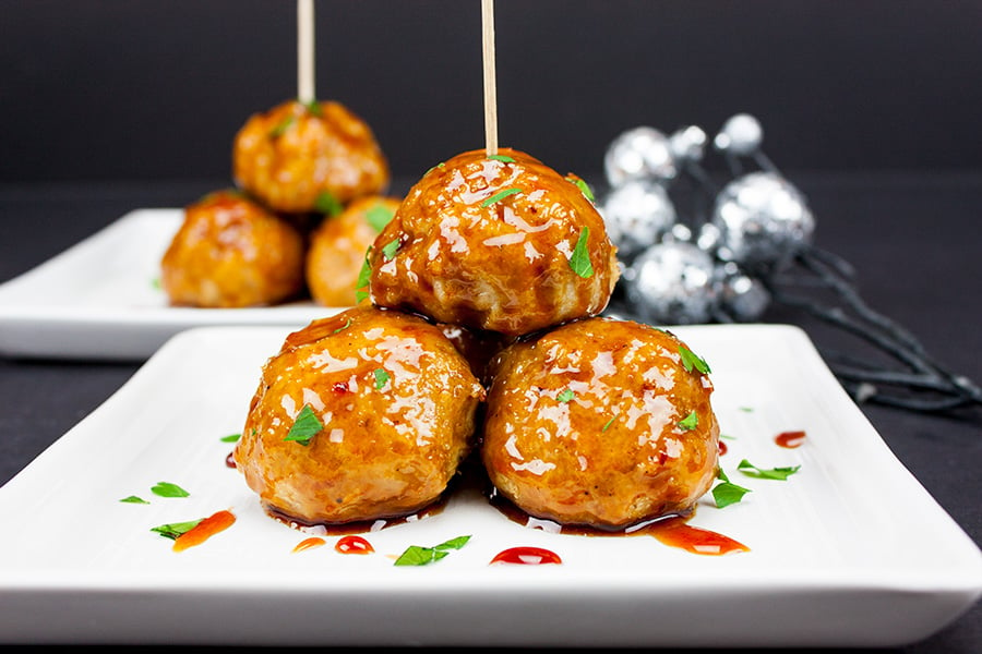 Firecracker Chicken Meatballs on a square white plate garnished with sauce and parsley