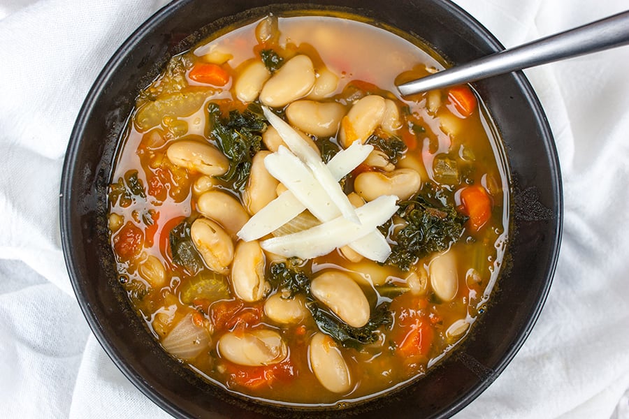 Tuscan white bean soup in a black bowl, garnished with shaved parmesan.