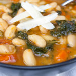 Tuscan White Bean Soup with a parmesan cheese garnish in a dark bowl.