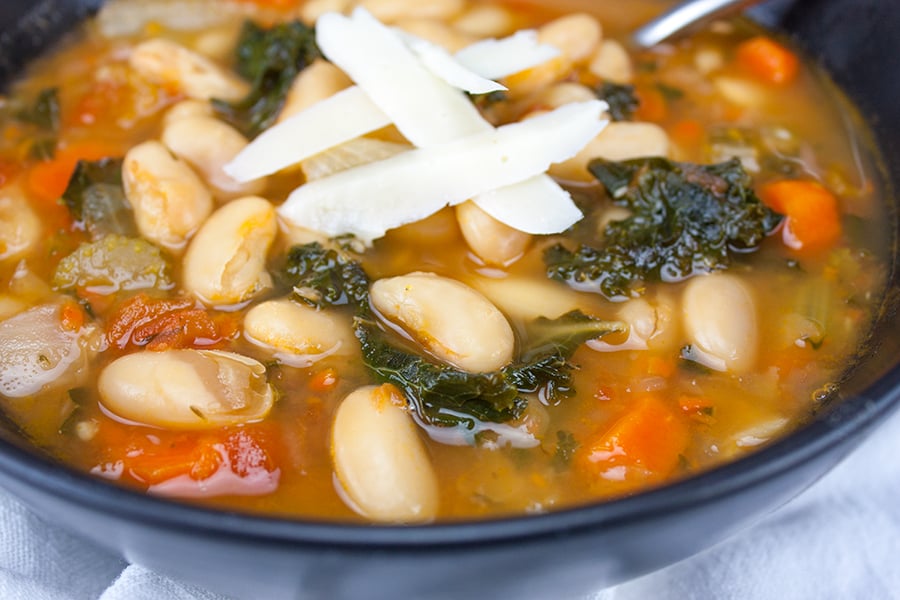 Tuscan White Bean Soup with a parmesan cheese garnish in a dark bowl.