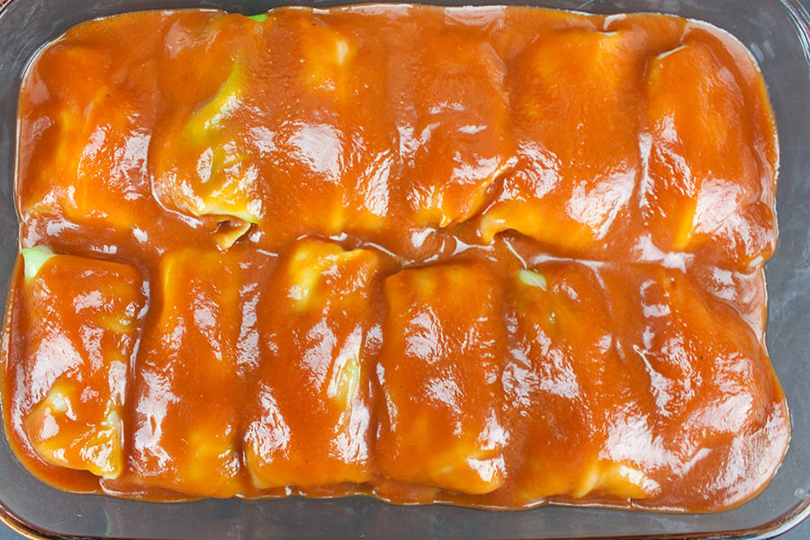 unbaked cabbage rolls covered in sauce in a glass baking dish