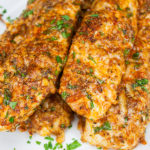 Parmesan crusted chicken tenders stacked on a light plate garnished with minced parsley.