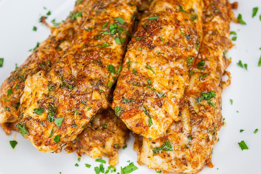 Parmesan crusted chicken tenders stacked on a light plate garnished with minced parsley.