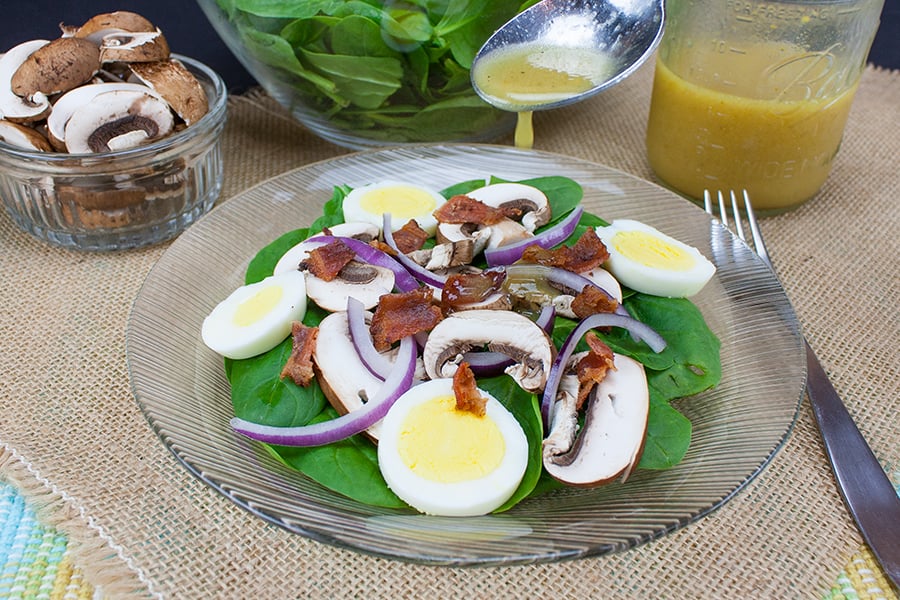 Spinach Salad with Curry Mustard Vinaigrette served on a glass plate.