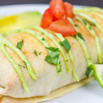 Baked Chicken Chimichangas garnished with cilantro, tomato, and lime wedges on a white plate.