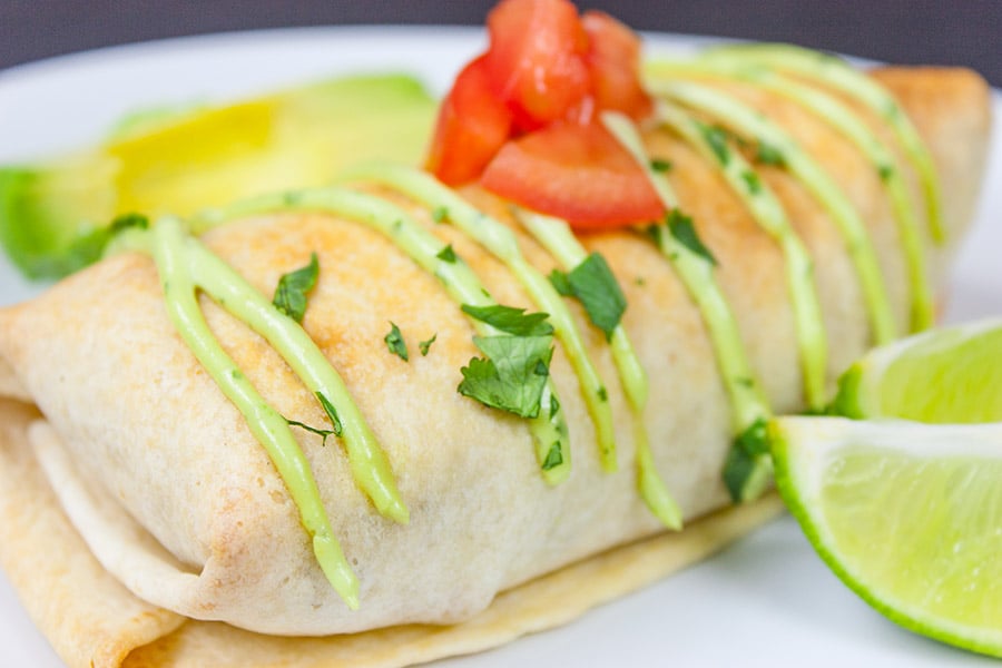 Baked Chicken Chimichangas garnished with cilantro, tomato, and lime wedges on a white plate.