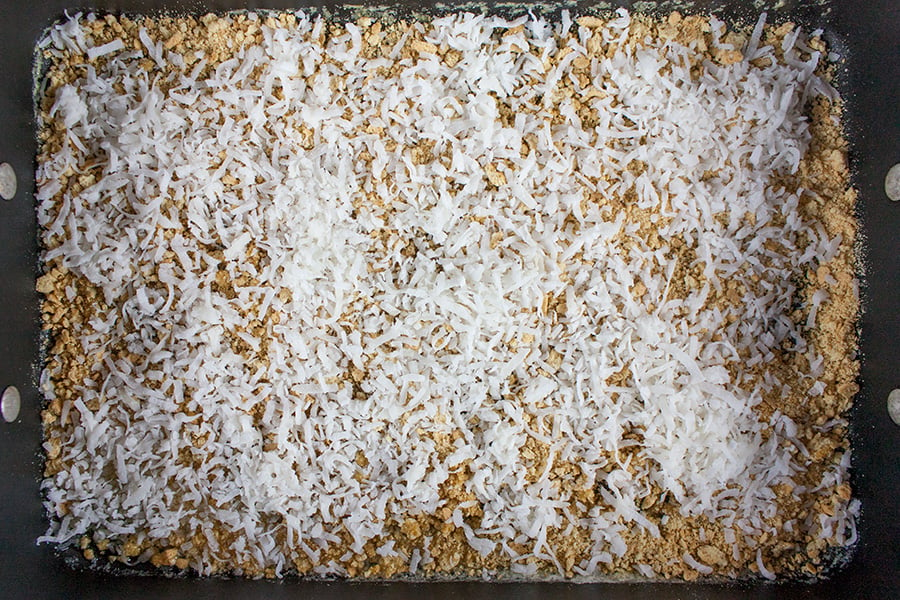 Classic Hello Dolly Cookies - graham cracker crumbs and coconut spread in a baking pan