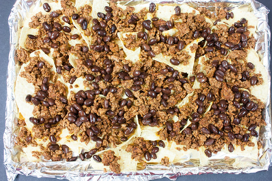 Tortilla chips, ground beef, and black beans on a foil lined baking sheet.