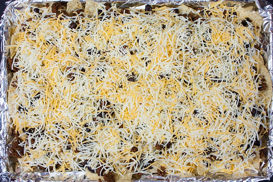 Tortilla chips, ground beef, black beans, and shredded cheese on a foil lined baking sheet.