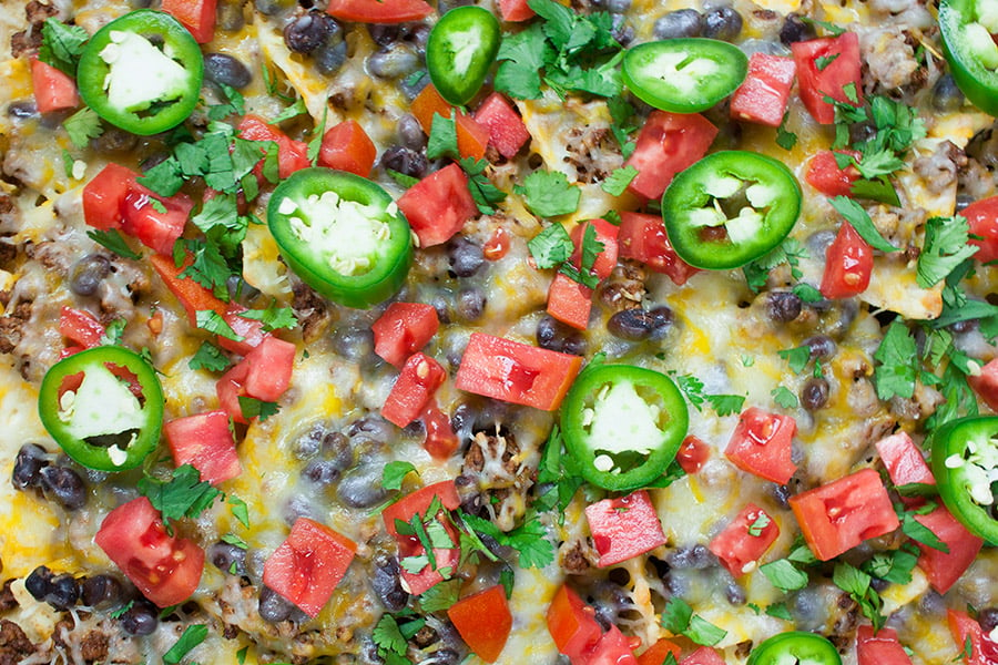 Sheet Pan Beef Nachos topped with tomatoes, green onions, jalapenos, and lime wedges.