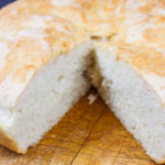 No Knead Skillet Bread on a wooden cutting board with a wedge cut out.