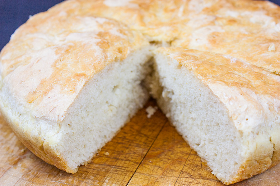 No Knead Skillet Bread on a wooden cutting board with a wedge cut out.