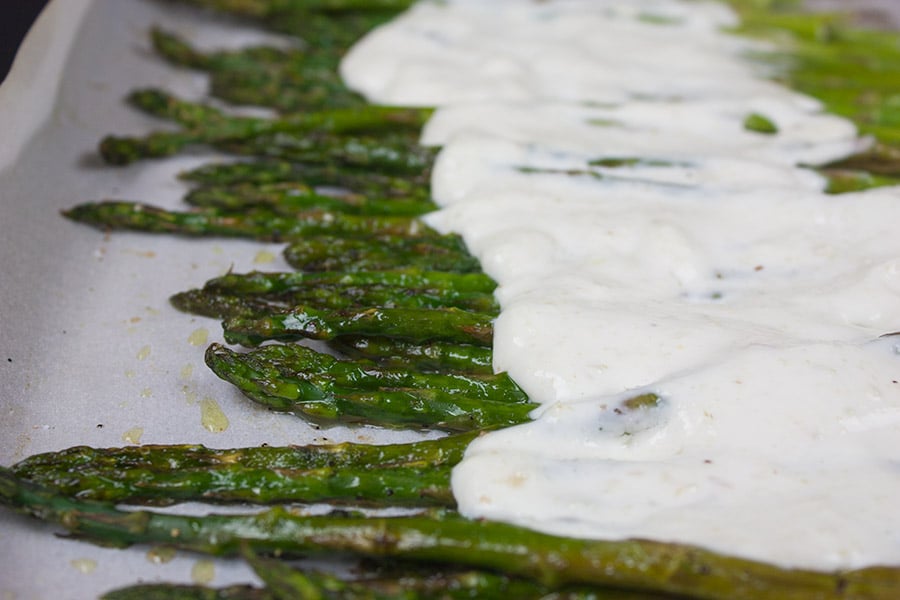 Asparagus with a horseradish cream sauce on a baking sheet pan.