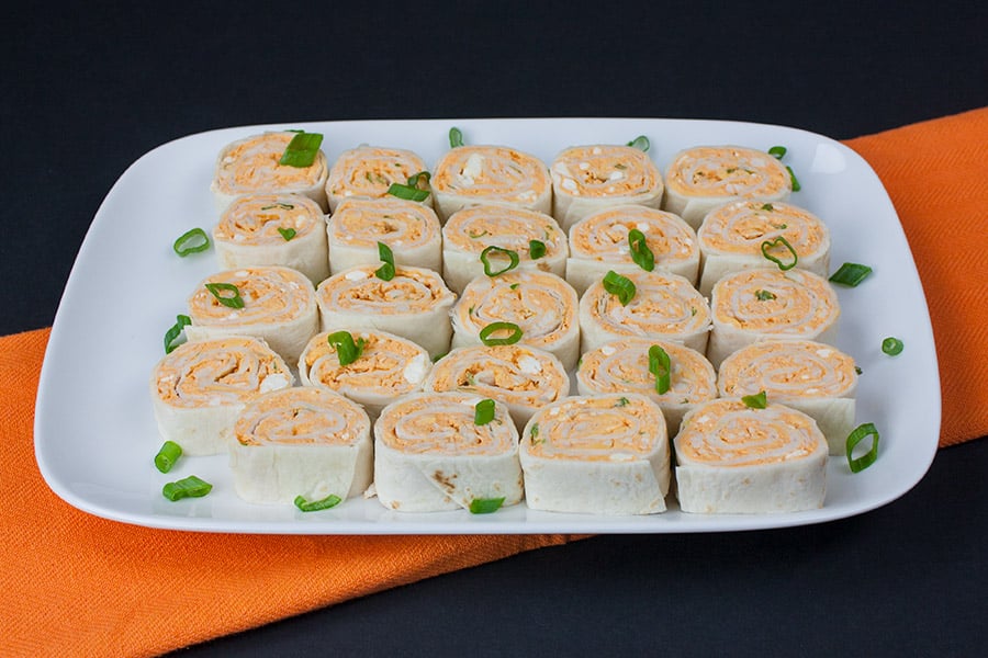 Buffalo Chicken Pinwheels on a platter garnished with diced green onions.