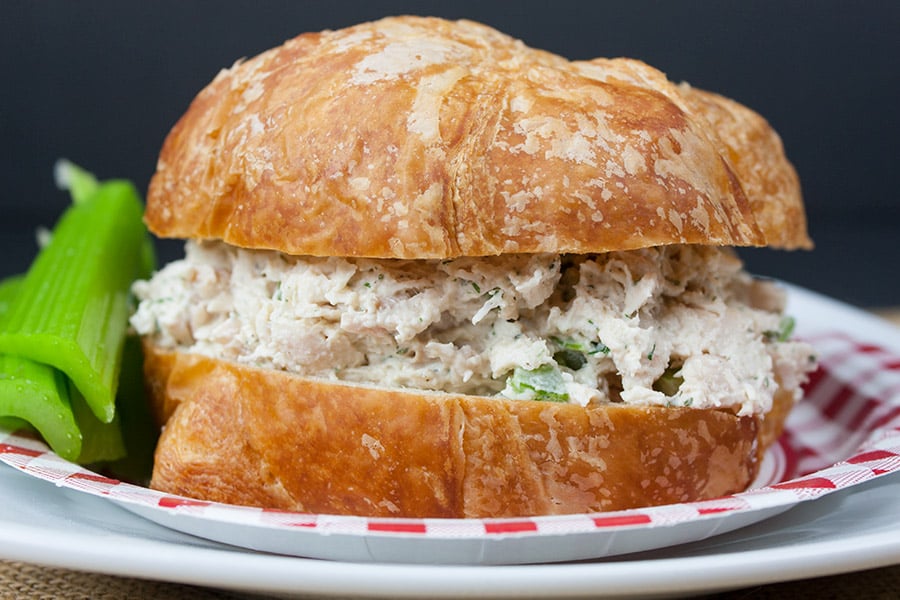 Savory Chicken Salad sandwich on a checkerboard paper plate with a celery garnish.