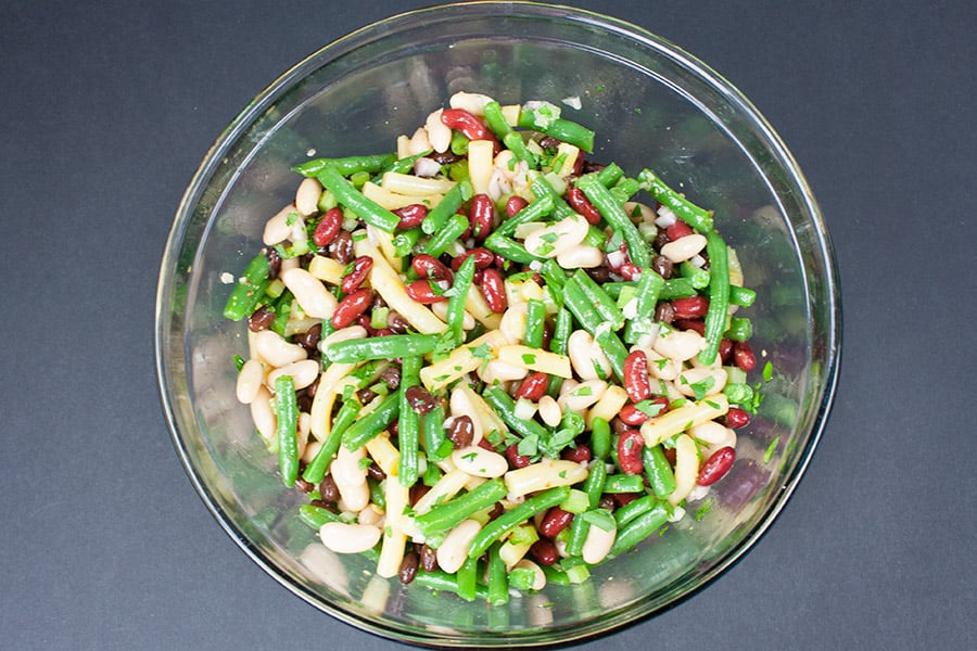 Five Bean Salad ingredients tossed with the dressing in a glass mixing bowl