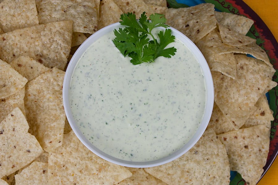 Creamy Jalapeno Cilantro Dip in a white bowl garnished with a sprig of cilantro and surrounded by tortilla chips