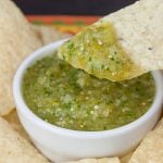 Dipping a tortilla chip into a bowl of salsa verde.