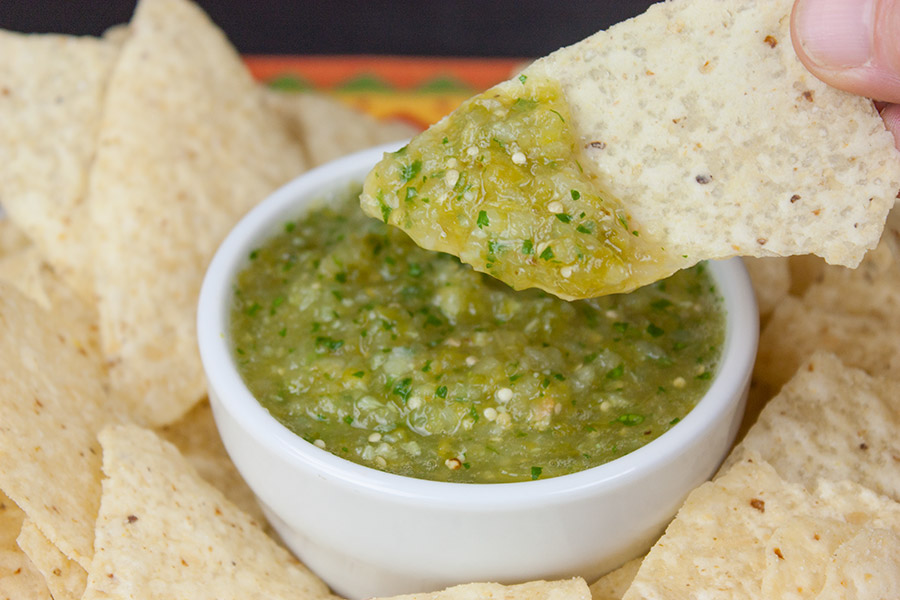 Dipping a tortilla chip into a bowl of salsa verde.