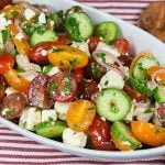 Tomato Cucumber Feta Salad in a white serving bowl on a red striped tablecloth.
