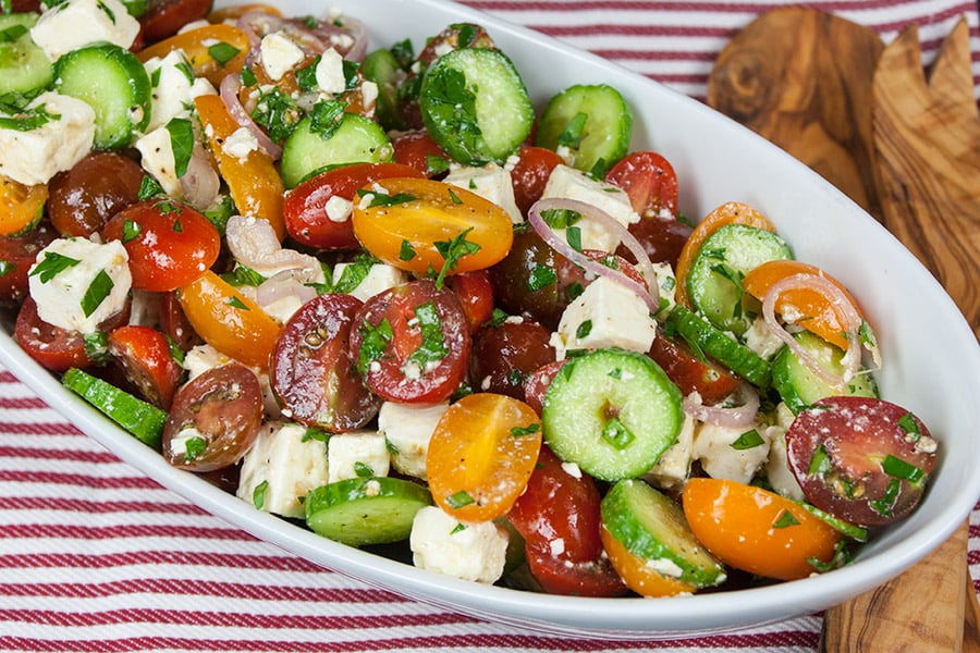 Tomato Cucumber Feta Salad in a white serving bowl on a red striped tablecloth.