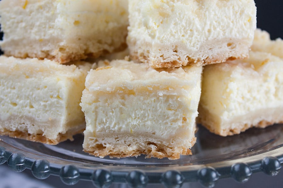 Lemon Cheesecake Shortbread Bars stacked on a glass cake stand