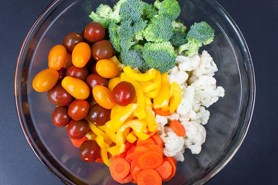 marinated fresh vegetable salad - tomatoes, broccoli florets, chopped bell peppers, diced carrots, and cauliflower florets in glass bowl