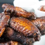 Amazing Smoked Chicken Wings piled high on a white platter with bbq sauce in the background.