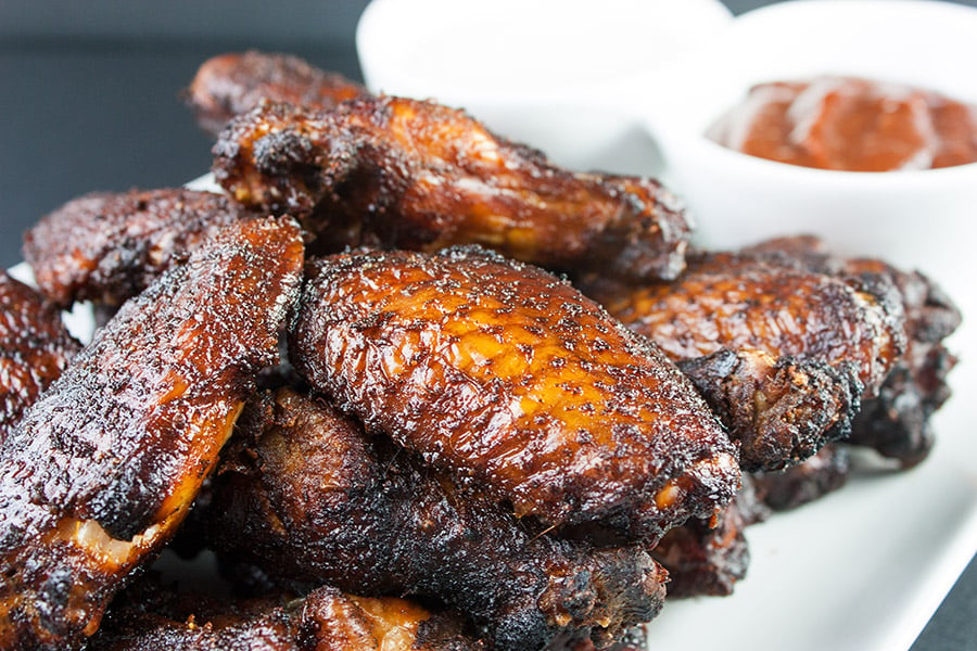 Amazing Smoked Chicken Wings piled high on a white platter with bbq sauce in the background.