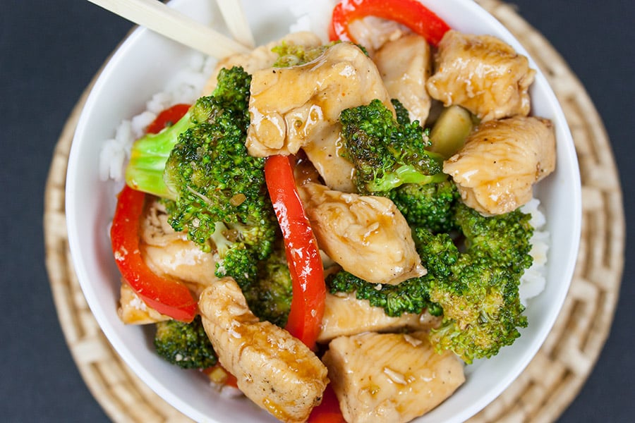 Easy Chicken and Broccoli Stir Fry over rice in a white bowl with chopsticks