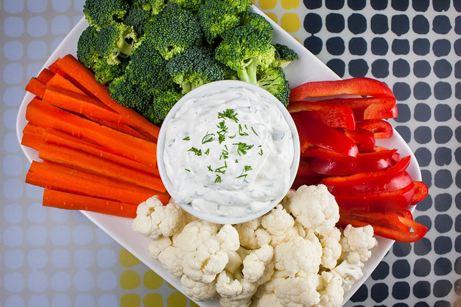 Fresh Herb Vegetable Dip in a white bowl surrounded by cut broccoli, cauliflower, carrots, and red bell peppers.