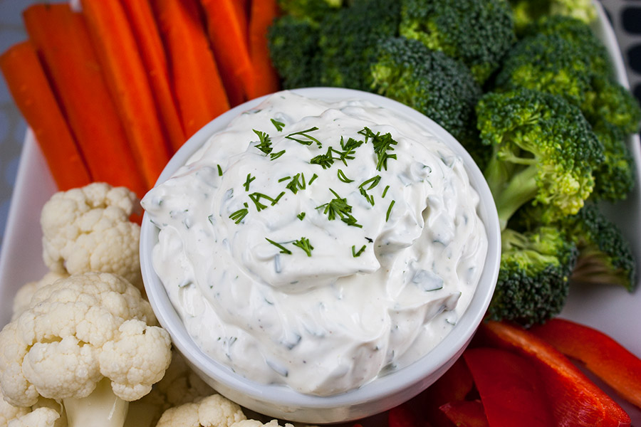 Fresh Herb Vegetable Dip in a white bowl surrounded by cut broccoli, cauliflower, carrots, and red bell pepper