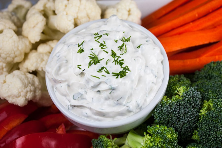 Fresh Herb Vegetable Dip in a white bowl surrounded by cut broccoli, cauliflower, carrots, and red bell pepper