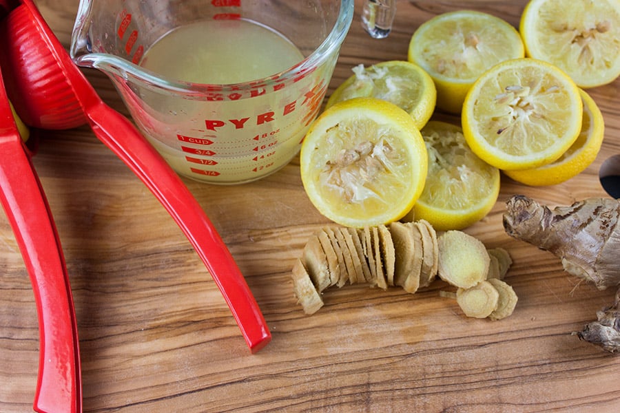 Honey Ginger Lemonade - juiced lemons, slice ginger and a measuring cup on a wooden cutting board