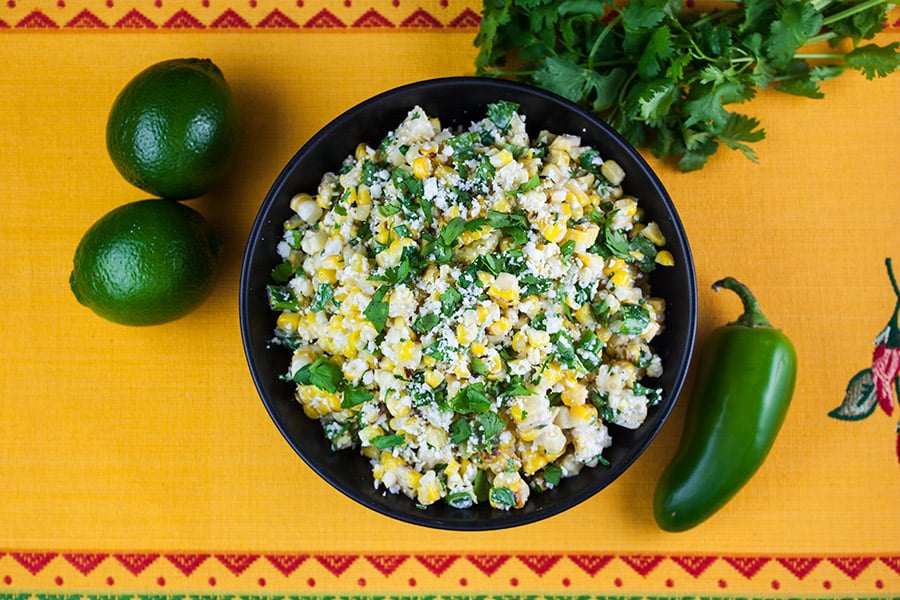 Grilled Mexican Street Corn Salad in a black bowl on a yellow back ground