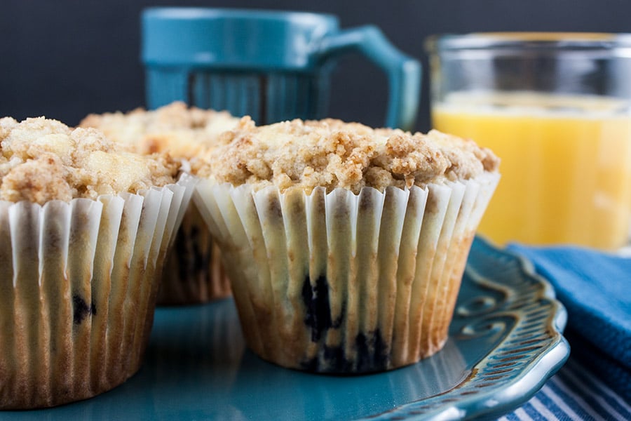 Lemon Streusel Blueberry Muffins on blue plate blue coffee mug orange juice in clear glass