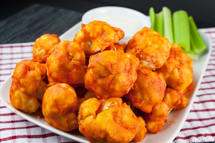 Buffalo cauliflower bites on a white plate with celery and ranch dressing.