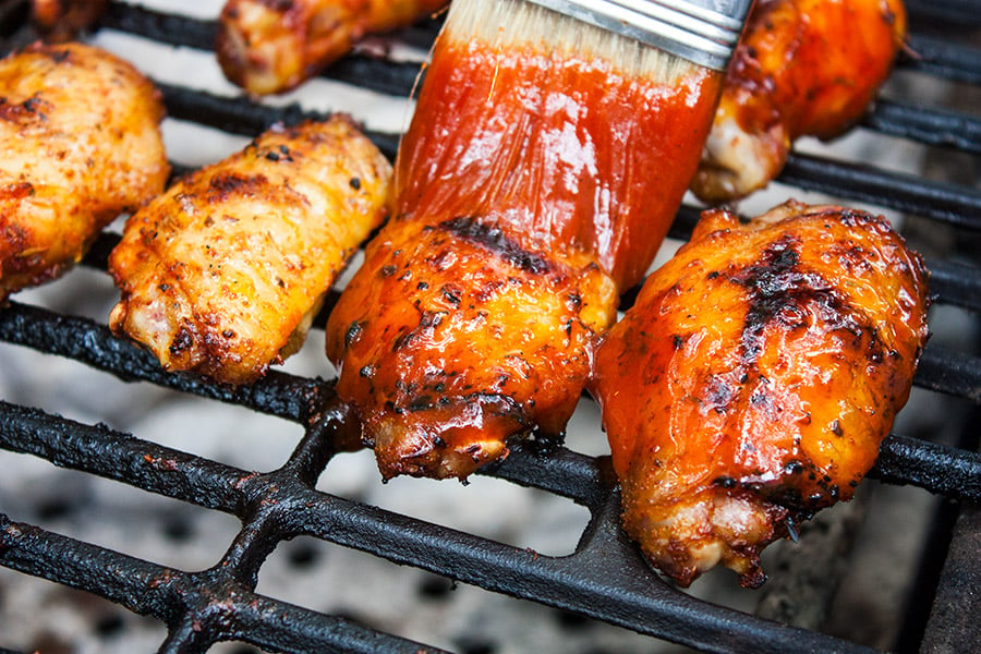 Cajun Smoked Wings on a grill with sauce being applied.