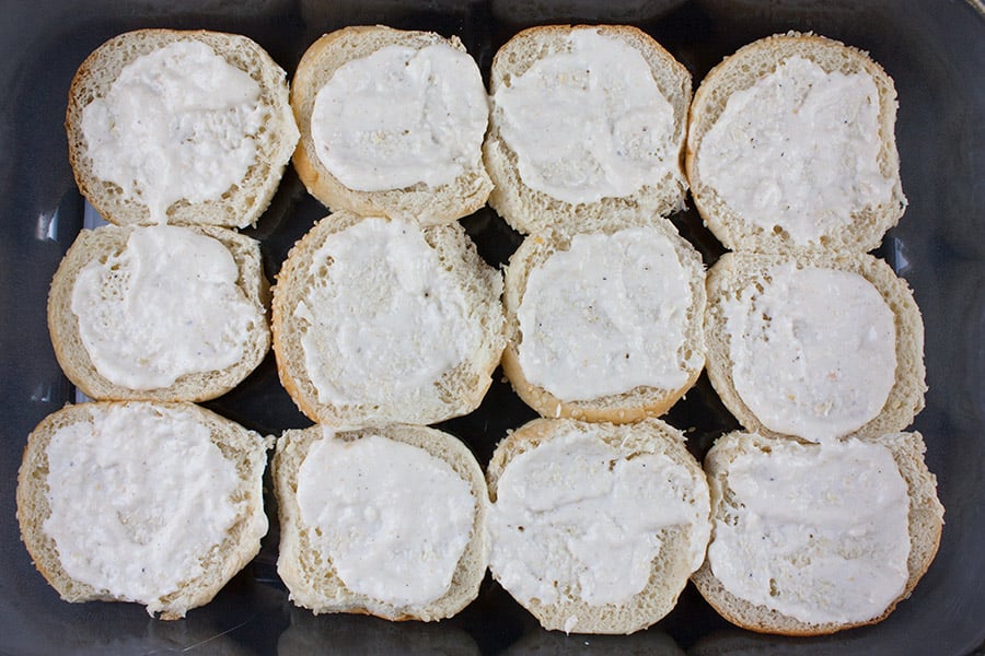 Horseradish sauce spread on bottom buns in a baking dish.