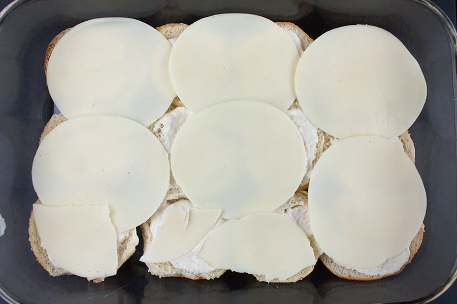 Cheese slices layered over the prepared bottom buns in a baking dish.