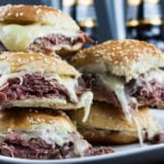 Roast beef sliders stacked on white plate beer bottles in background.